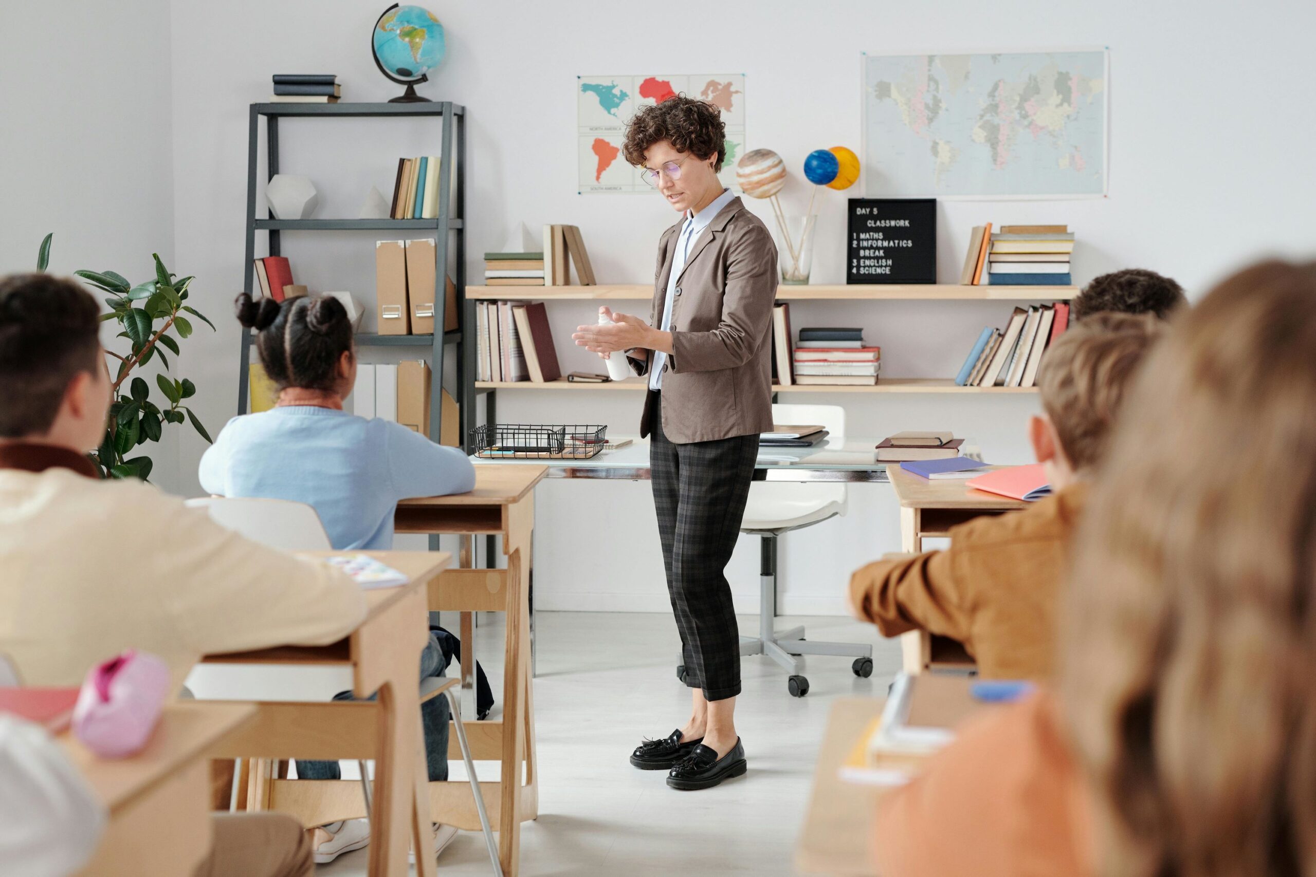 A female teacher is standing in front a classroom with students.