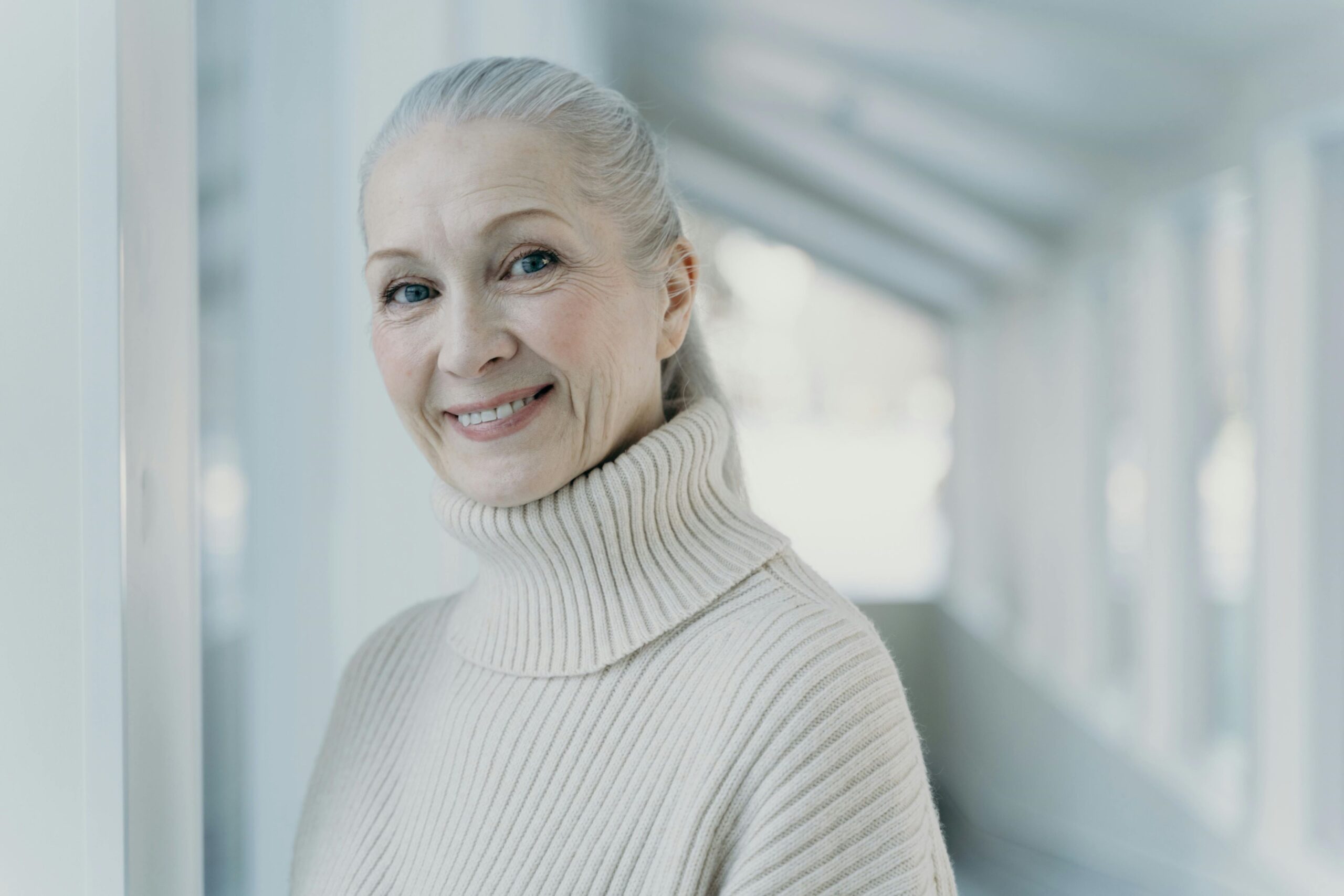 An elderly woman with gray hair dressed in a turtleneck sweater, reflecting a sense of comfort and experience.