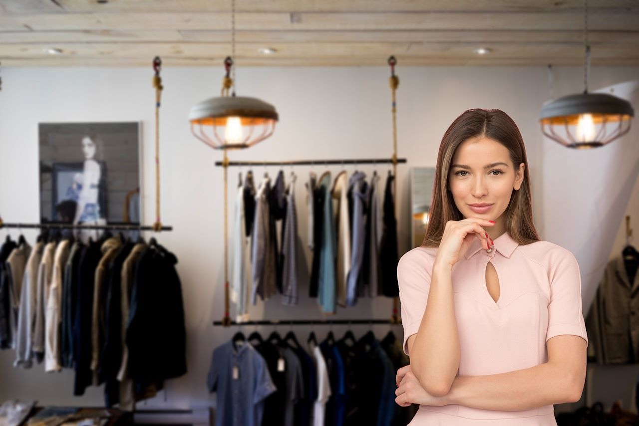 A female sole trader stands before a clothing rack, representing her fashion business.